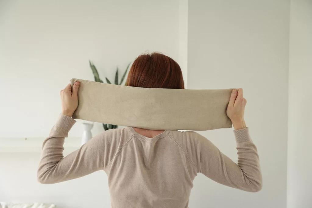 Femme avec une bouillotte en graines de lin cervicales autour du cou 
